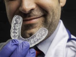 Caucasian dentist showing an orthodontic transparent dental aligner - concept for dental treatment